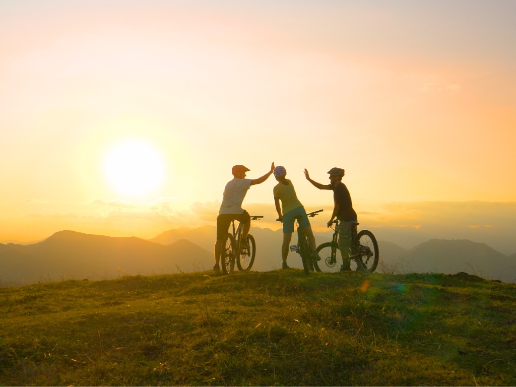 Mountain biking friends high-fiving after reaching the summit at sunrise